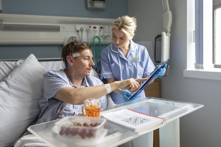 Female nurse caring for a patient in hospital while he is having a brain study done to investigate his sleep seizures. He is staying at a medical establishment in the North East of England  and has multiple electrodes monitoring his scalp. The nurse is showing him a clipboard with information.

Videos are available similar to this scenario.